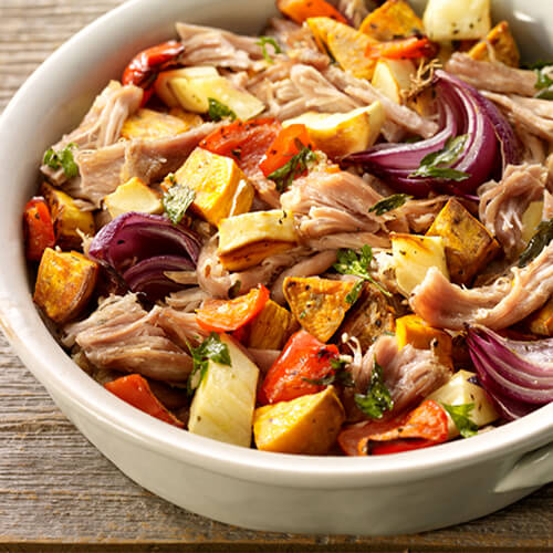 Rustic roasted turkey pot roast and vegetables in a white dish on a wood table.