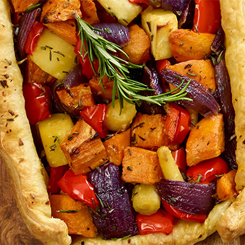 A puff pastry filled with sweet flavors of onion, parsnips, bell pepper, and sweet potatoes, served on a wooden board on a black and white tablecloth.