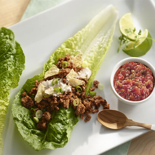Lettuce wraps filled with a hearty portion of turkey and cilantro, served with a tasty sour cream and salsa dipping sauce, on a white platter.