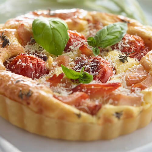 Savory tomato and turkey tarts garnished with basil on a white plate.