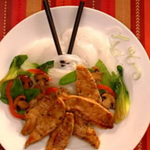 Savory turkey tenderloins, fresh veggies, baby bok choy all on top of delicate rice noodles, on a white plate, with a red tablecloth.