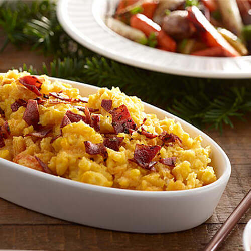 Bacon corn casserole topped with crumbled bacon in a white serving dish.