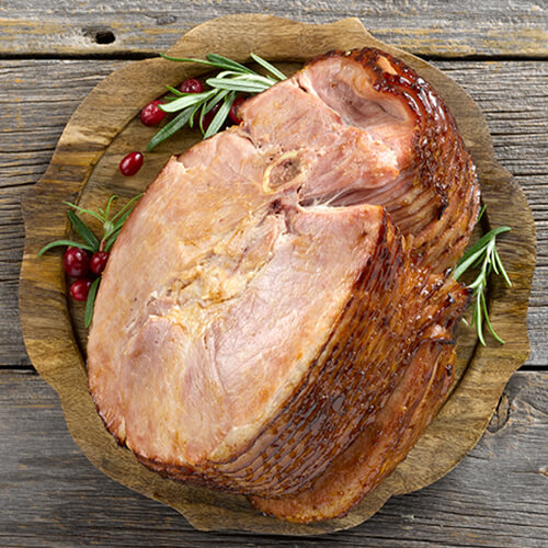 Slow cooker holiday ham garnished with sprigs of rosemary on a wood plate.