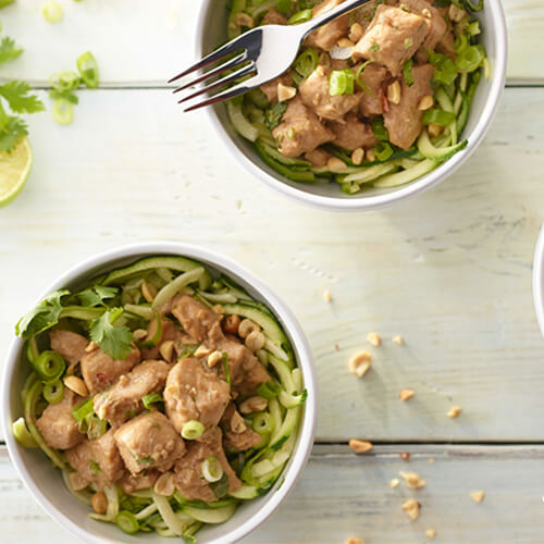 Two white bowls of Thai peanut turkey and zucchini noodles on a white wooden background.