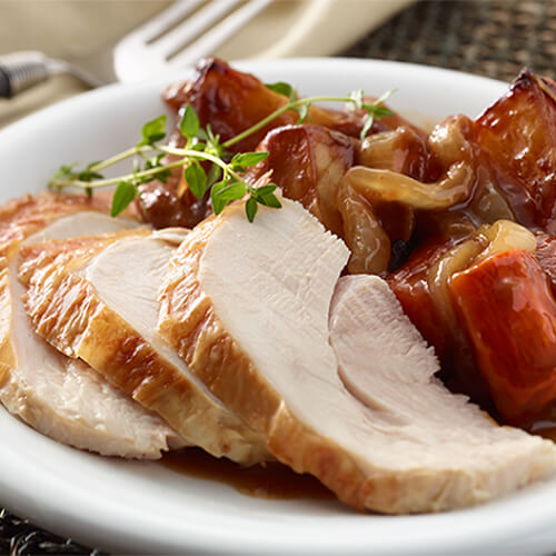 Juicy sliced turkey served with potatoes, onion, carrots, and gravy, on a white plate.