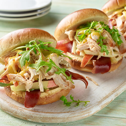 Smoked turkey burger with apple slaw garnished with green onion on a white tray.