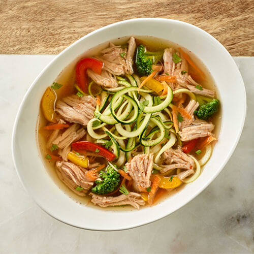 Smoky turkey and zucchini ramen noodles on a white bowl on a marble table.