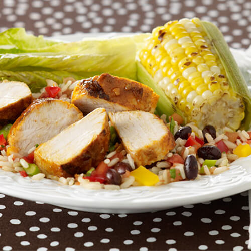 Brown rice, black beans, bell peppers, cilantro and salsa served over grilled turkey tenderloins, lettuce and a corn cob, on a white plate atop a polka dot tablecloth.