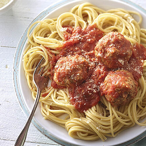 A heaping portion of spaghetti, homemade marinara sauce, and turkey meatballs with a side of parmesan cheese on a white plate and a wooden table.
