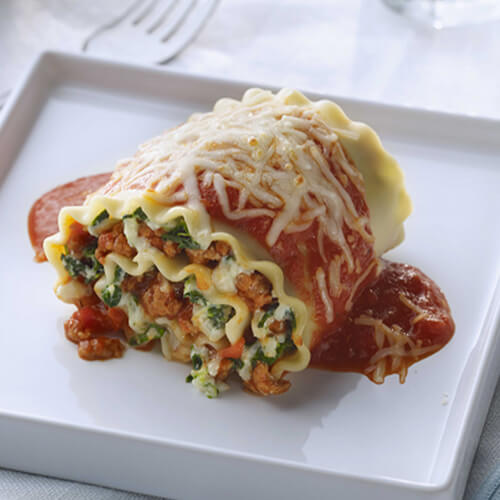 Rolled lasagna noodles filled with ricotta cheese, spinach, and JENNIE-O® lean ground turkey, topped with ricotta cheese and tomato sauce on a white plate.