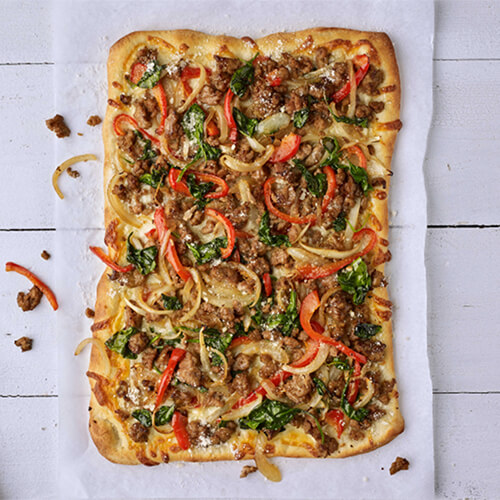 Rectangular flatbread pizza topped with turkey sausage, red peppers, spinach and cheese.
