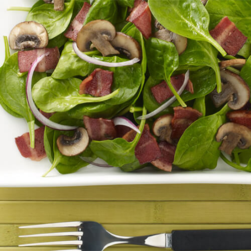 Spinach, JENNIE-O® Turkey Bacon salad on a white plate.