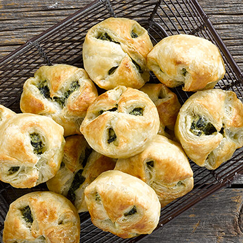 Spinach puffs stacked in a wire basket on a grey wood table.