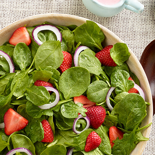 Creamy buttermilk dressing paired with juicy strawberries and crisp spinach, in a wooden bowl on a linen tablecloth.