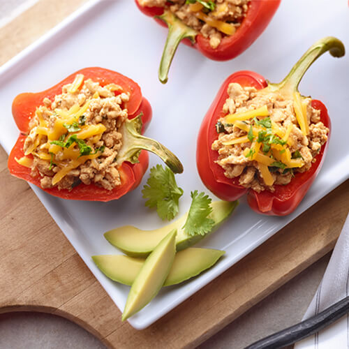 Colorful bell peppers filled with sautéed onion lean ground turkey, and topped with melted Cheddar, served on a white tray on a wooden pizza board and a white table