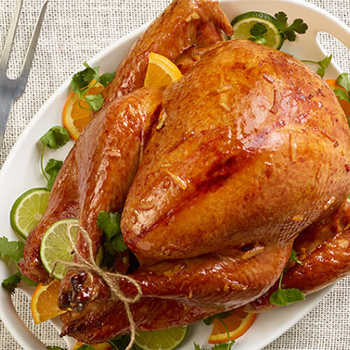 A citrus, honey and ginger glaze atop roasted turkey garnished with herbs and fruits atop a linen tablecloth.