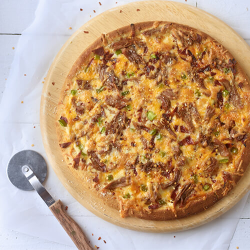 Sweet chili turkey pizza on a wood plate sitting on a white wood table.