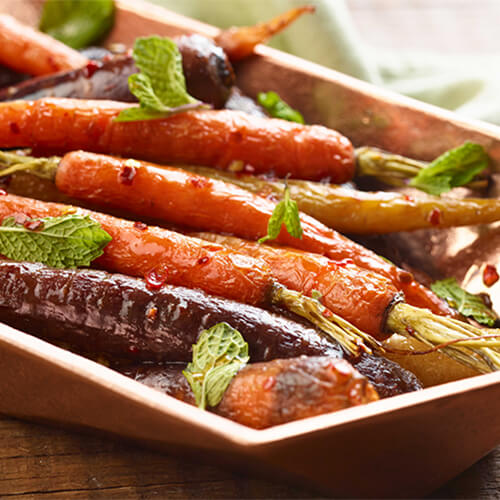 Sweet honey chili glazed carrots garnished with mint on a white tray.