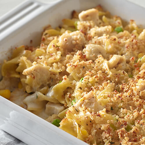 Soft egg noodles, leat turkey breast cutlets, with peas, celery, and corn in a baking dish and topped with breadcrumbs.