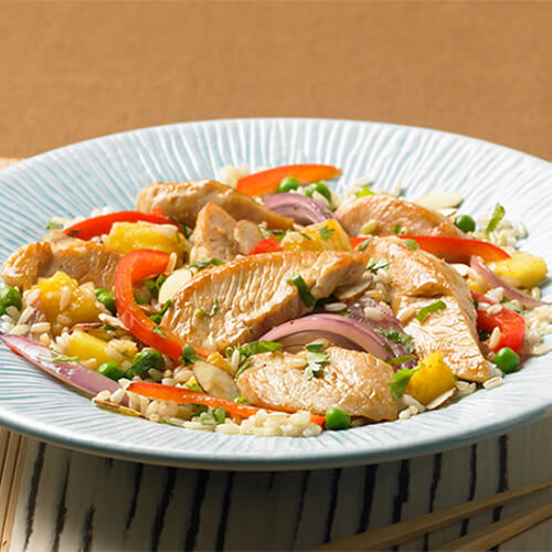 Stir-fry turkey strips and skilleted vegetables drizzled in teriyaki sauce, and served over rice on a blue painted plate, on a brown bamboo-style placemat and a linen tablecloth.