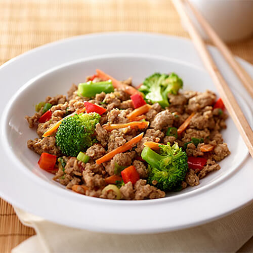 White bowl of teriyaki turkey topped with broccoli and red bell peppers.