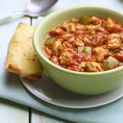 Tex mex turkey chili in a green bowl with a side of bread.