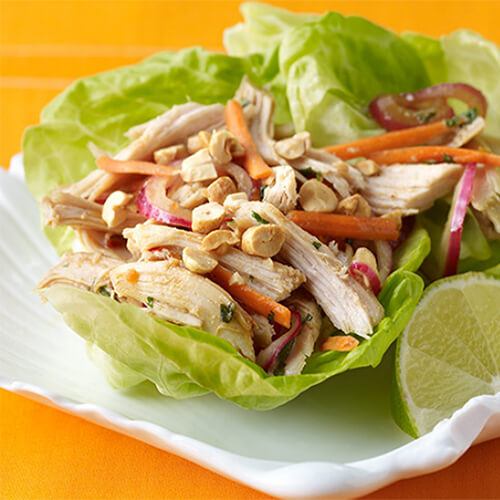 A flavorful lettuce wrap filled with turkey, peanuts, and vegetables, served with a lime wedge, on a white plate.