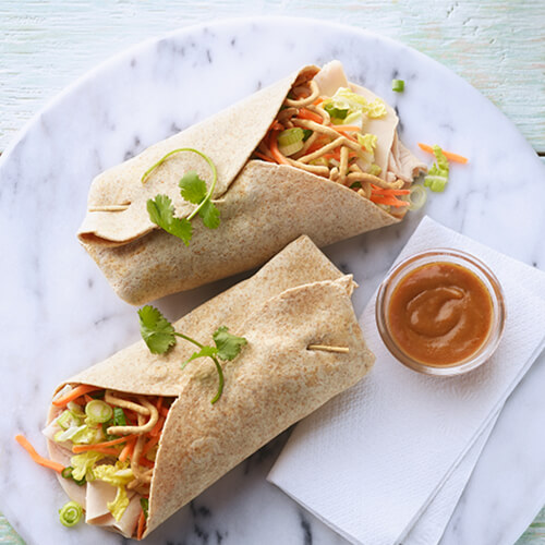 Thai wraps filled with turkey, fresh veggies, and chow mein noodles, served with peanut sauce on a marble plate.