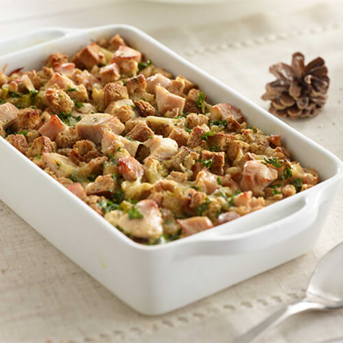 Thanksgiving breakfast egg strata casserole in a white baking dish next to a pinecone.