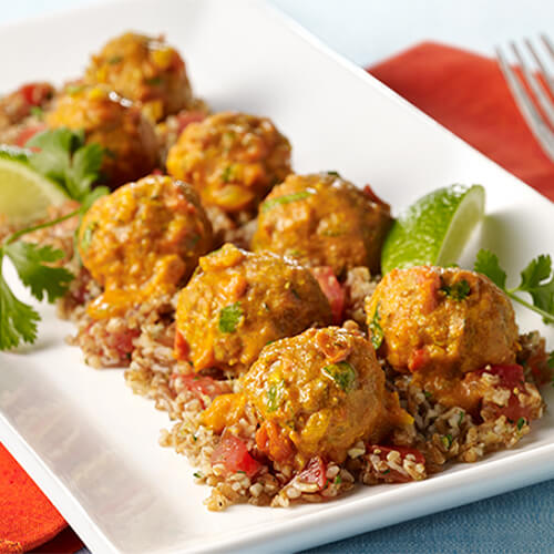 Savory homemade turkey meatballs on a bed of bulgur wheat, topped with a creamy-spicy Tikka Masala sauce and garnished with cilantro and lime on a white platter atop a red napkin.