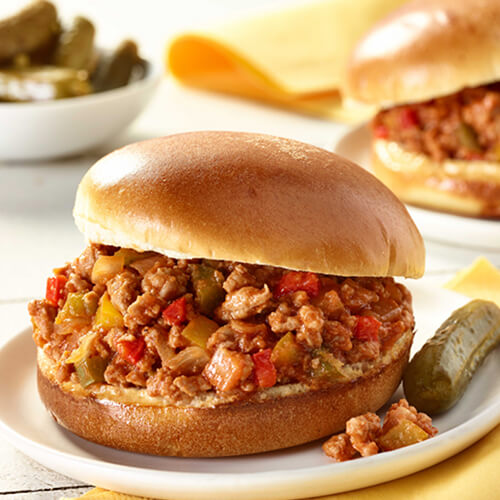 Chopped turkey meat mixed with red, green, and yellow bell pepper on a white plate next to a small pickle.