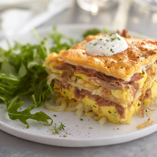 Hash brown lasagna stuffed with eggs and herbs, topped with sour cream next to a bed of arugula.