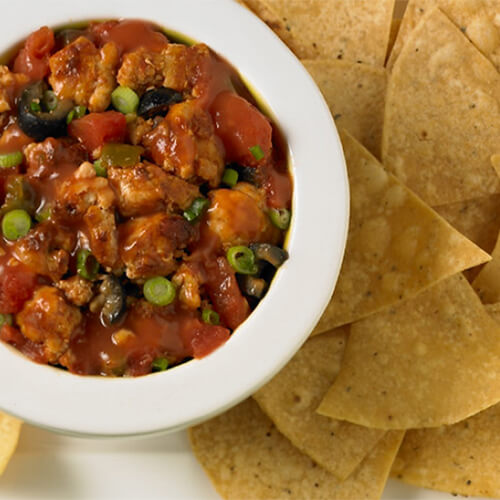 A salsa made out of lean ground turkey, vegetables, and salsa in a bowl, with a large portion of chips on a white background.