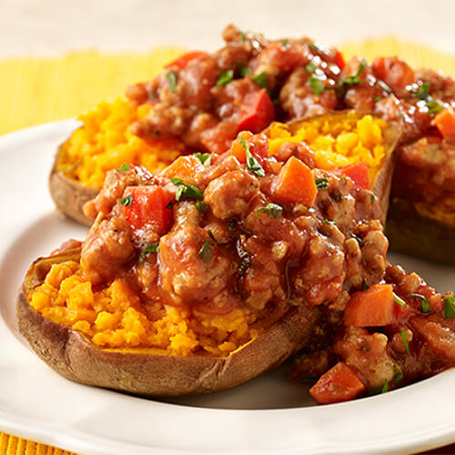 Sweet potatoes filled with turkey, tomato sauce, and more sloppy joe fixins, served on a white plate.