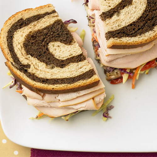 A turkey sandwich on marbled pumpernickel bread next to taro chips on a white plate.