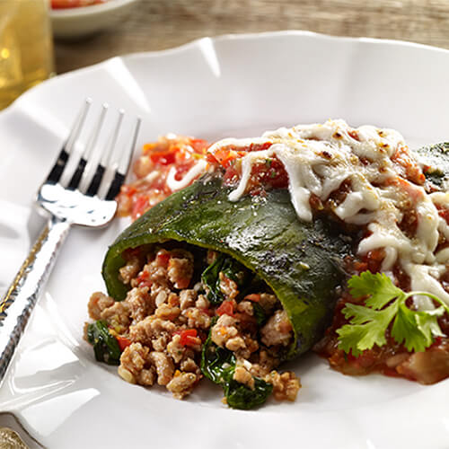 Grilled Poblano peppers stuffed with seasoned ground turkey and baked with a fresh homemade tomato sauce and cheese, served on a white plate.