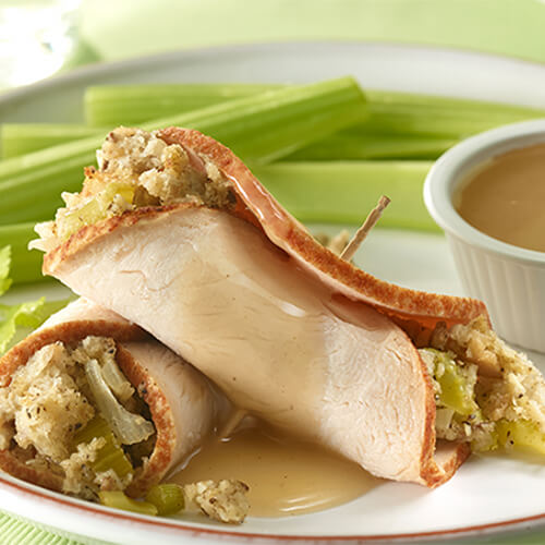 Delicious bit sized roll ups filled with turkey, stuff, and celery, topped with a warm gravy on a white plate.