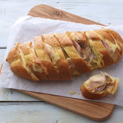 Melted Swiss cheese and hickory smoked turkey baked into a baguette served with grain mustard on a cooking board on parchment paper on a wooden table.