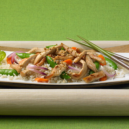 Crunchy carrots, pea pods, a ginger on a bed of rice and topped with JENNIE-O® Turkey strips on a white plate.