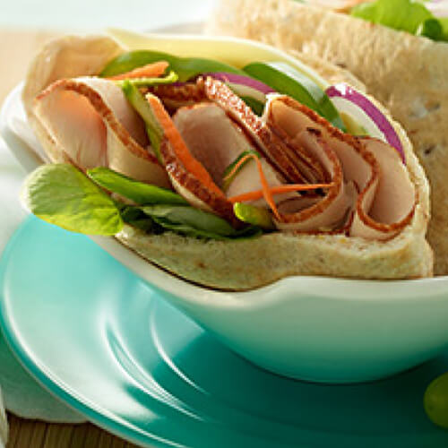 Pita pockets loaded with fresh spinach, zucchini, carrots, green pepper and lean turkey breast filled with chipotle mayo and served on a blue bowl, with a side of grapes.