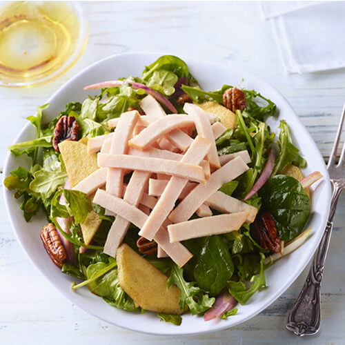 Lean turkey breast, tart Granny Smith apples, glazed pecans, and topped with a spicy sweet dressing, served on a white plate.