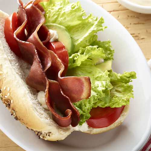 Turkey bacon, lettuce, and tomato on a bun on a white plate.