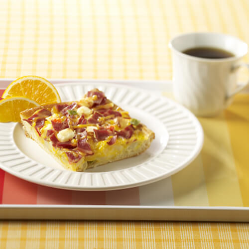 Flaky crescent roll crust baked in eggs, crispy turkey bacon, hash browns and cheese, served on a white plate with a side of coffee on a colorful platter.