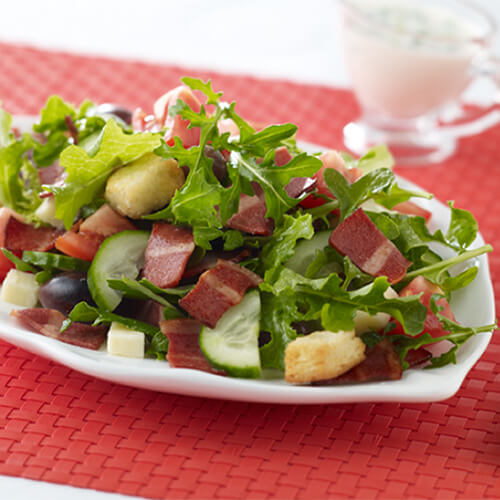 A bunch of leafy greens with JENNIE-O® Turkey Bacon and tomatoes.