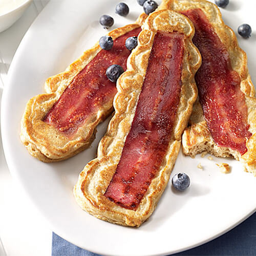 Bacon strip filled pancakes served with blueberries and syrup, served on a white plate.