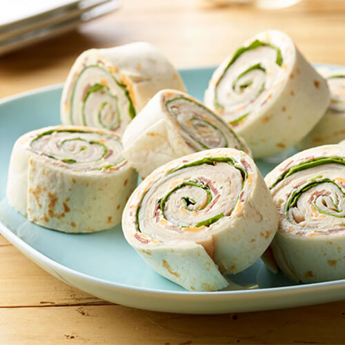 Turkey bacon rollups stacked on a blue plate on a wood table.