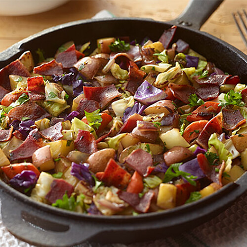 JENNIE-O® turkey bacon, red potatoes, sautéed vegetable such as green and red cabbage, parsley, and onion all in a hot skillet.