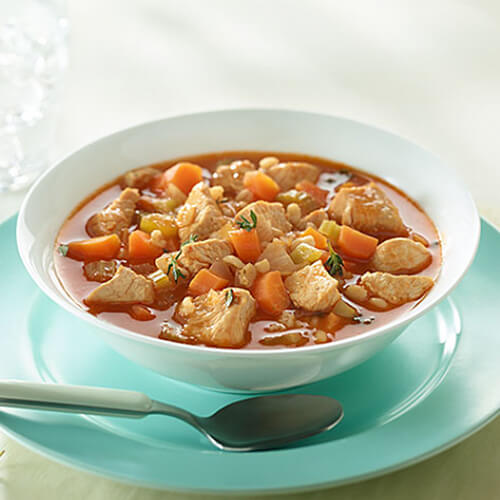 Lean turkey and barley soup filled with carrots, celery and fresh thyme, served on a white bowl with bread and a blue plate.