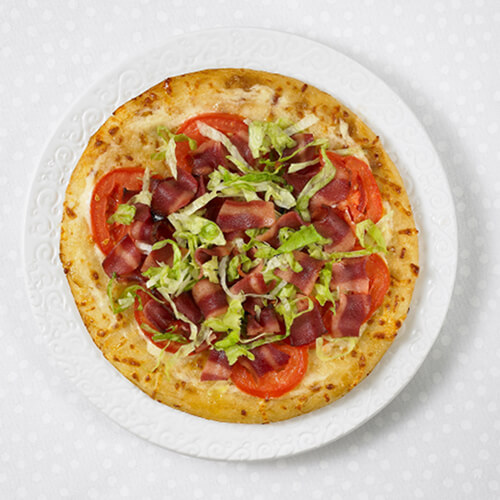 Homemade pizza topped with tomatoes, lettuce, and JENNIE-O® Turkey Bacon on a white plate.