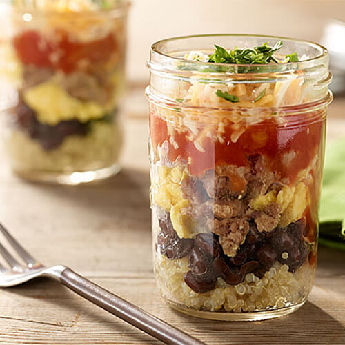 Rice, beans, eggs, turkey, salsa, and cheese, served in a mason jar on a wooden table.